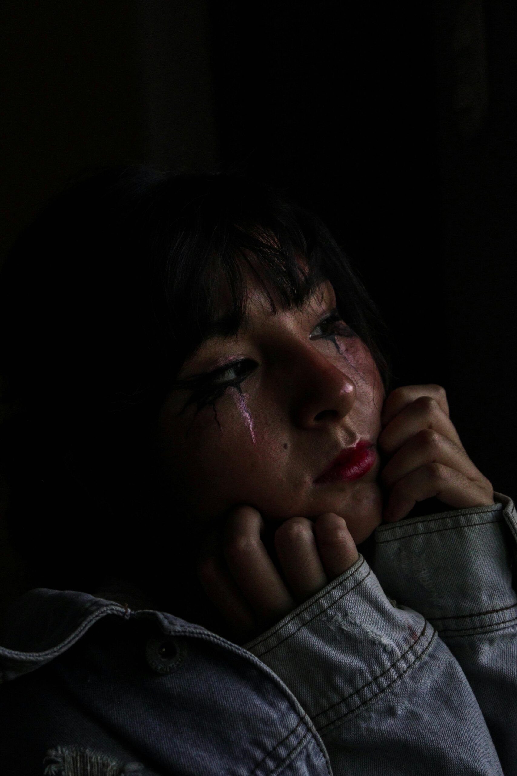 Moody portrait capturing a woman with tear-streaked makeup in low light, conveying sadness.